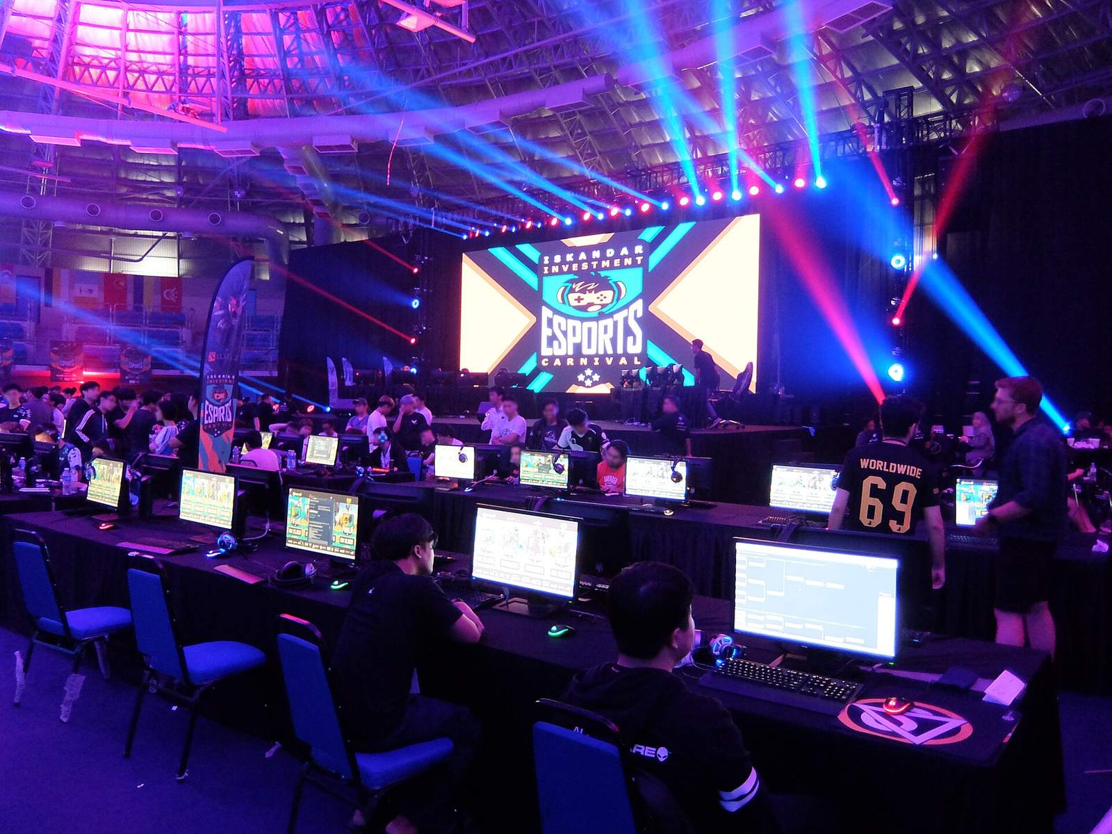 Esports tournament hall, players at PCs under stage lights, Malaysia